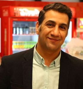 محمد نادری در یک سوپرمارکت با کت مشکی و پیراهن آبی