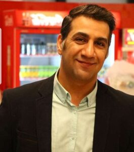 محمد نادری با کت مشکی و پیراهن سفید در یک سوپرمارکت